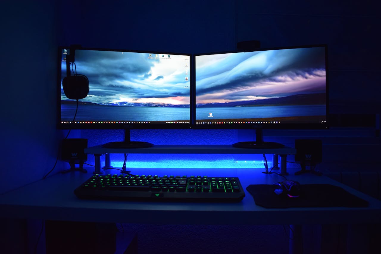 Services Dual monitors with blue lighting on a gaming desk setup.